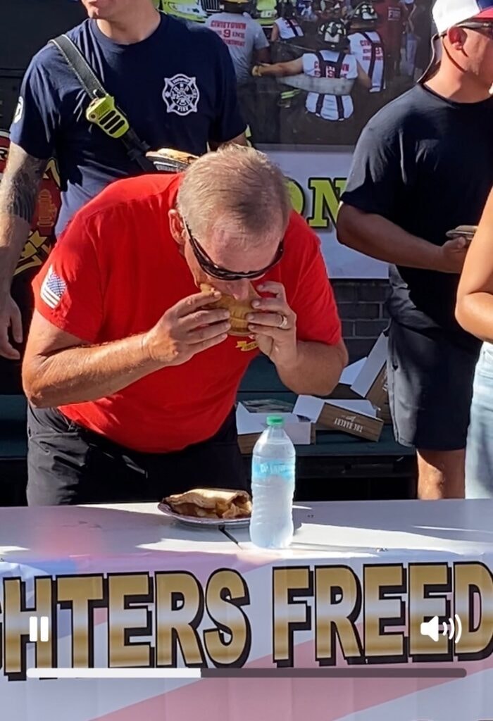 SJFD volunteer in red shirt competes in the eating contest at the Firefighter Freedom Competition