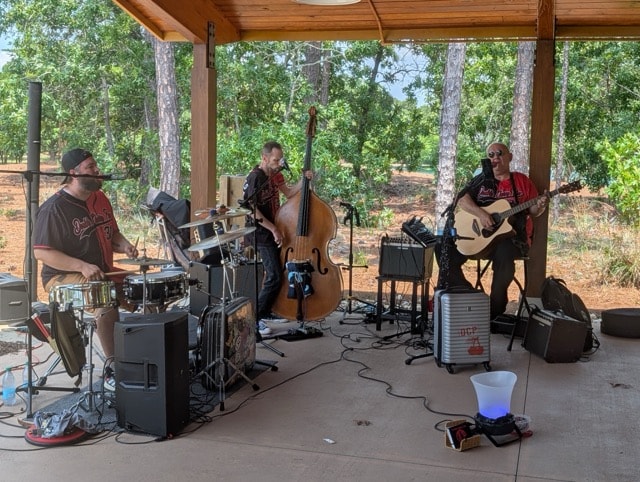 Double Cherry Pie — a three-piece band with drums, upright bass, and acoustic guitar — performs under the open-air pavilion at the SJFD picnic