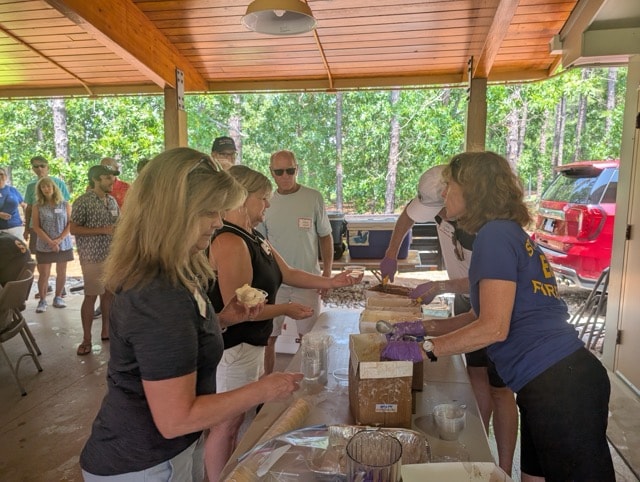 Volunteers and guests line up for Chuck's homemade ice cream served from a table at the edge of the pavilion