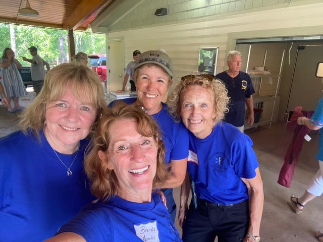 Four SJFD women volunteers in blue shirts take a selfie at the Woodlands Park Pavilion picnic